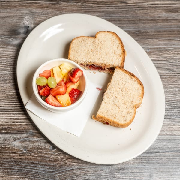 Peanut butter and jelly sandwich with a side of fresh fruit salad on a white plate.