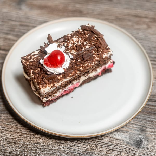 Black Forest cake slice with chocolate, cream, and a cherry on a white plate.