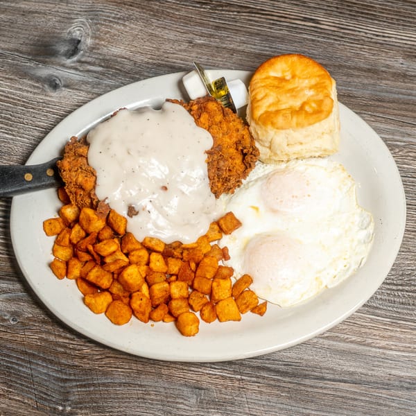 Chicken fried steak with gravy, home fries, two fried eggs, and a biscuit with butter.