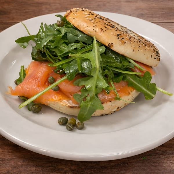 Everything bagel with smoked salmon, cream cheese, arugula, and capers on a white plate.