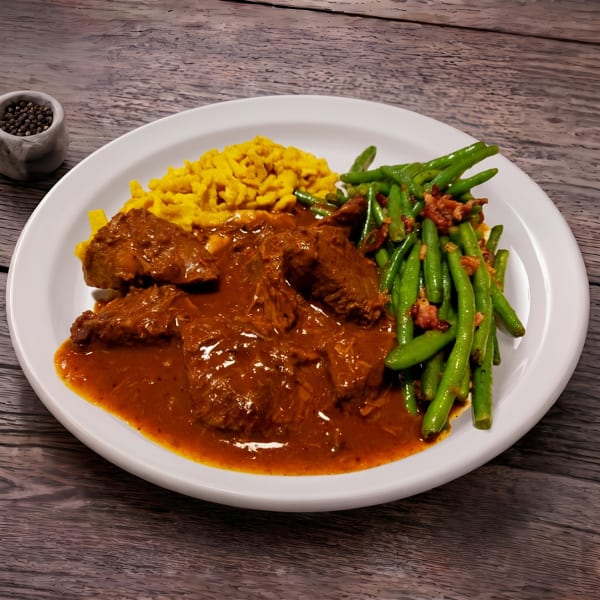 Hearty goulash with spaetzle and green beans topped with bacon bits on a white plate.