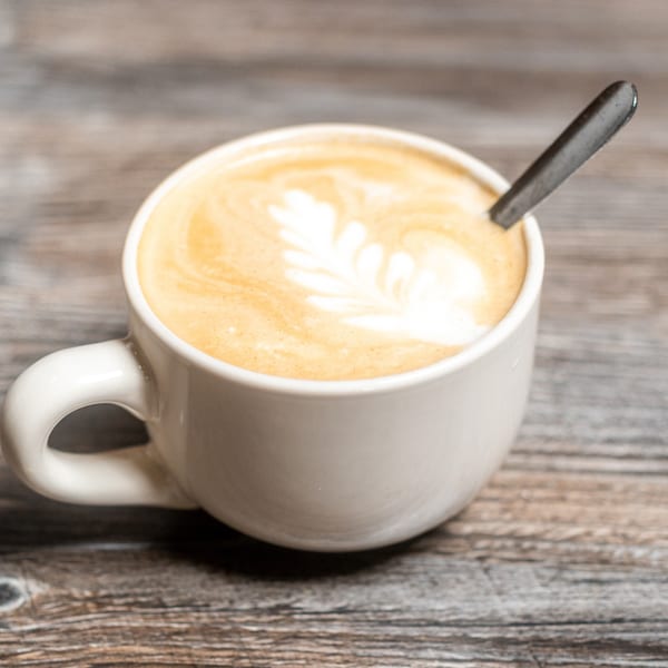 White cup of latte with leaf art and a spoon on a rustic wooden table.