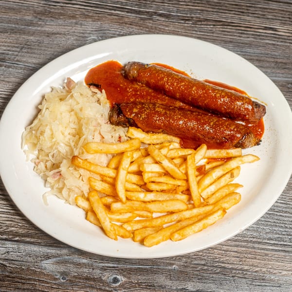 Currywurst sausages with red sauce, a side of sauerkraut, and golden french fries on a white plate.