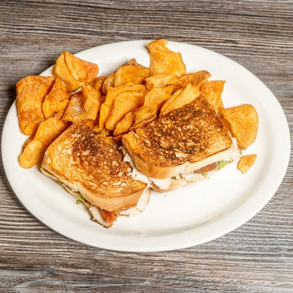Grilled sandwich cut in half with a side of golden potato chips on a white plate.