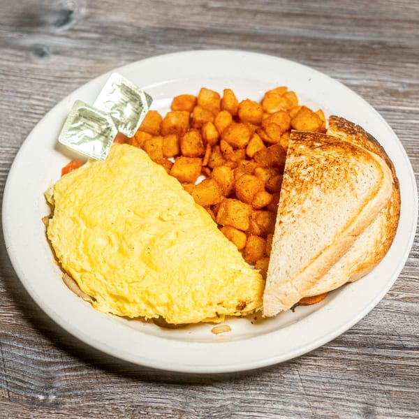 A breakfast plate with a fluffy omelet, crispy home fries, and two slices of toast.