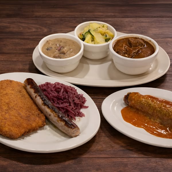 A German feast with schnitzel, bratwurst, red cabbage, currywurst, mushroom gravy, beef goulash, and potato salad.