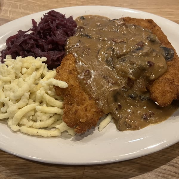 A plate of schnitzel with mushroom gravy, spaetzle, and red cabbage on a wooden table.