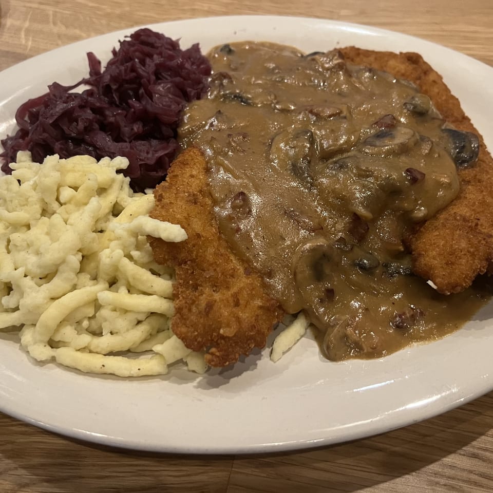 A plate of schnitzel with mushroom gravy, spaetzle, and red cabbage on a wooden table.