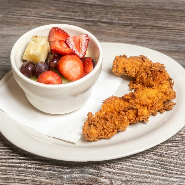Two crispy fried chicken tenders and a fruit cup with strawberries, grapes, and pineapple on a white plate.